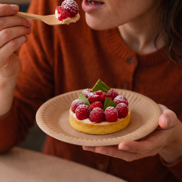 Persona comiendo una tartaleta de frambuesa en un plato de postre kraft