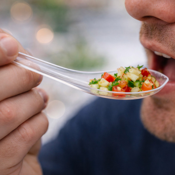 Una persona comiendo un vaso de vino con forma de cuchara de plástico