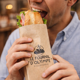 Hombre comiendo un bocadillo con una bolsa personalizada de una panadería